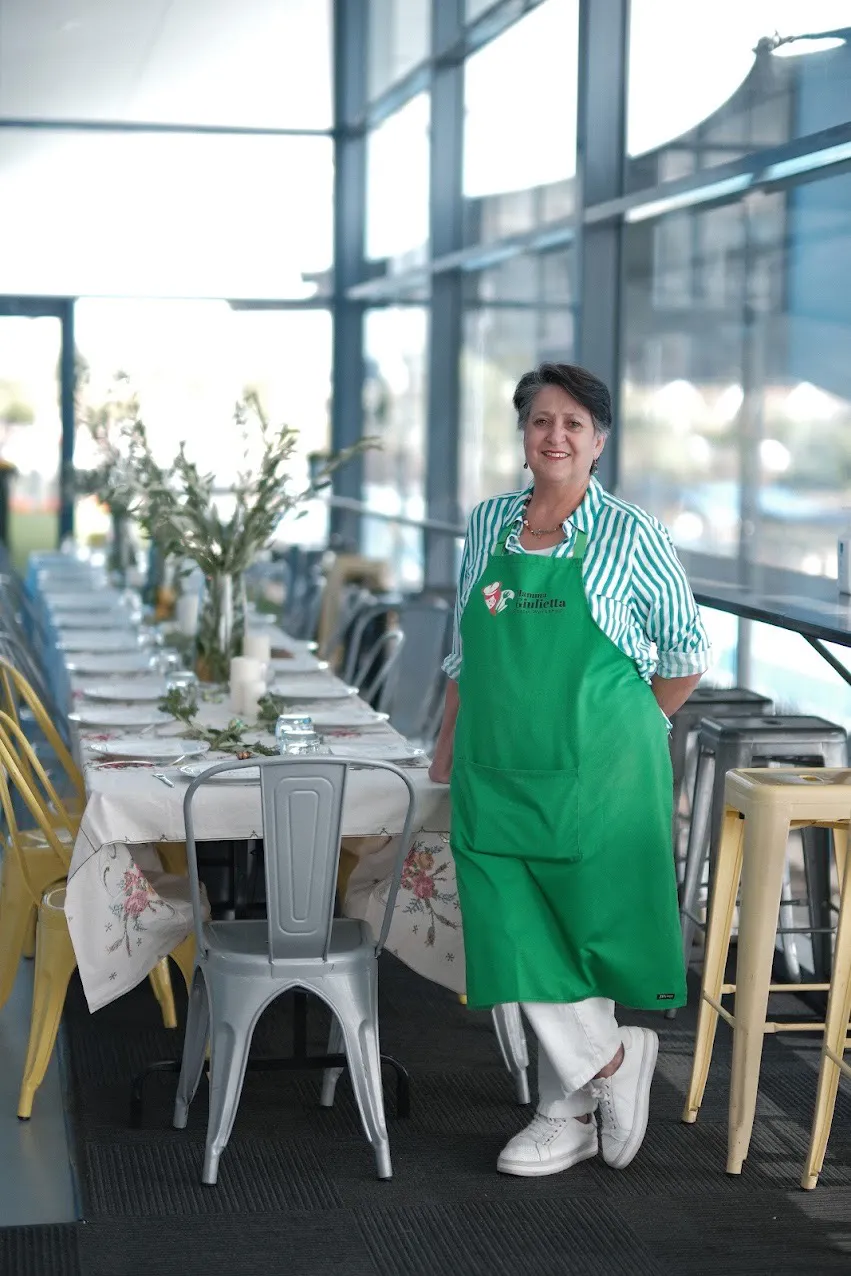 Mamma Giulietta standing beside a long table set for a team lunch